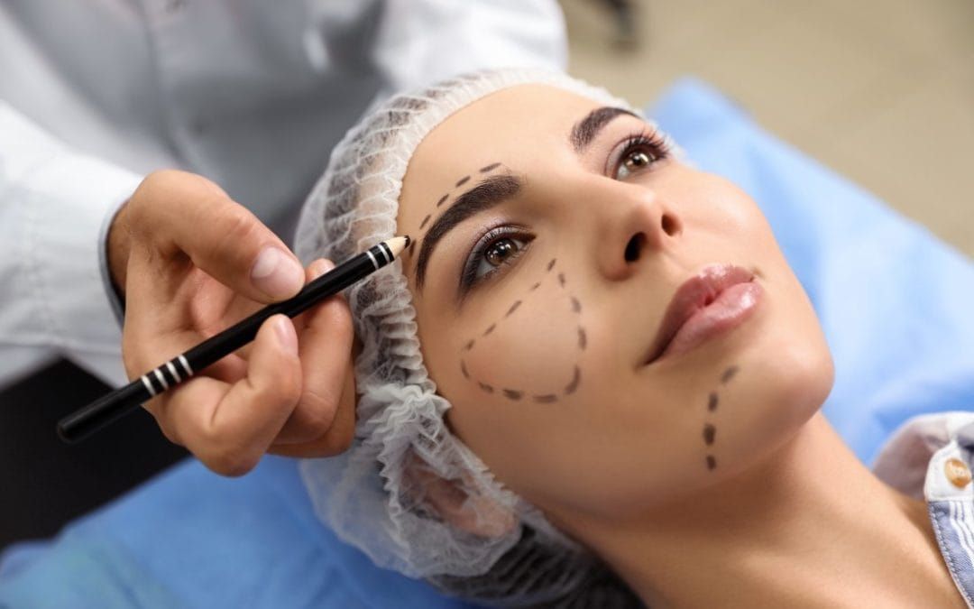 Un chirurgien esthétique marque le visage d'une femme au crayon avant une intervention.