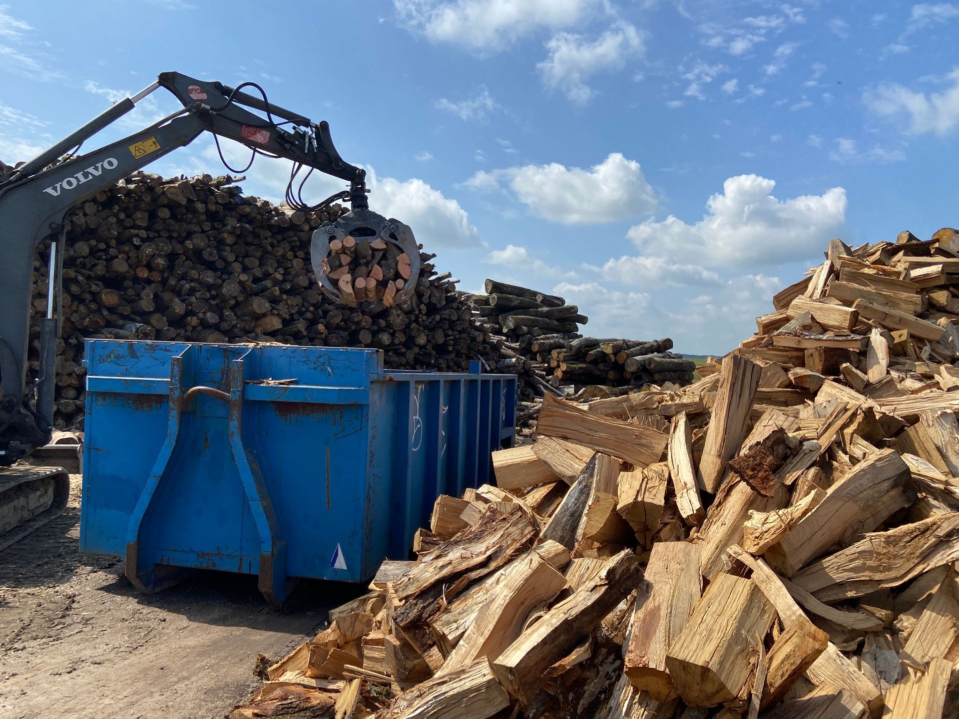 Des stères de bois chargés dans une benne par une pince mécanique