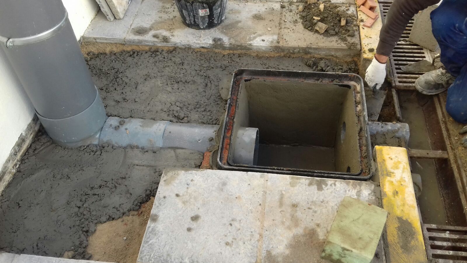Un hombre está colocando hormigón en el suelo al lado de una tapa de alcantarilla.