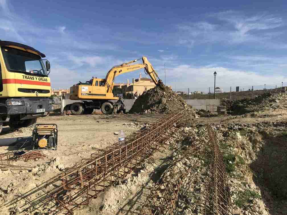 Una excavadora amarilla está moviendo tierra en un sitio de construcción al lado de un camión.