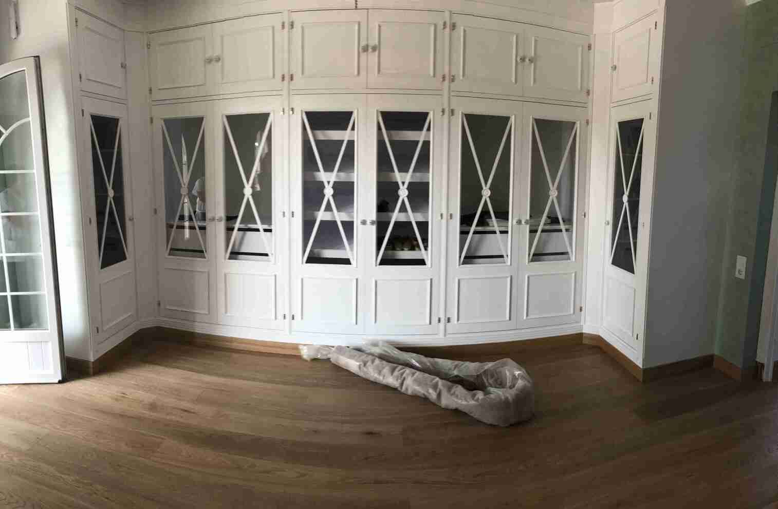 Una habitación con muchos gabinetes blancos y piso de madera.