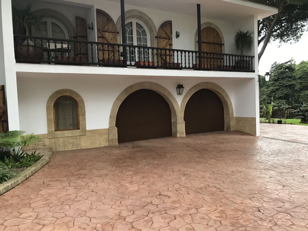 Una gran casa blanca con puertas de garaje arqueadas y una entrada de ladrillo.