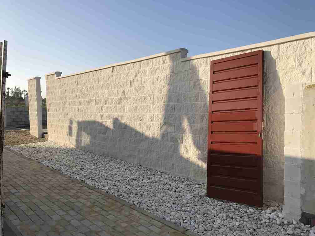 Una pared de ladrillo blanco con una puerta roja delante de ella.