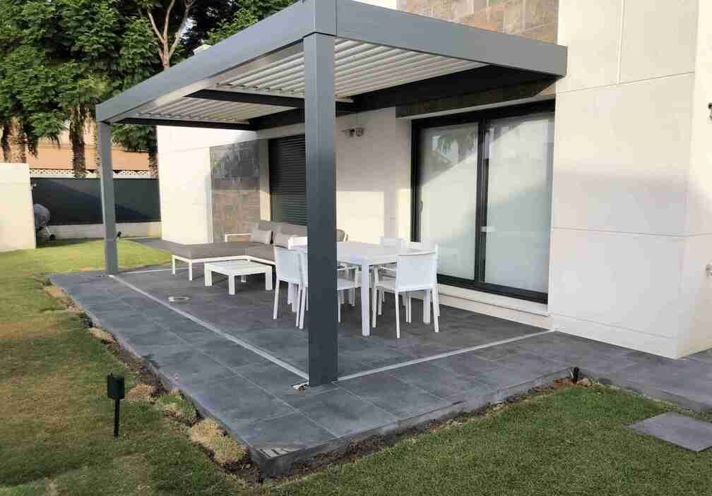 Un patio con una mesa y sillas debajo de una pérgola en el patio trasero de una casa.