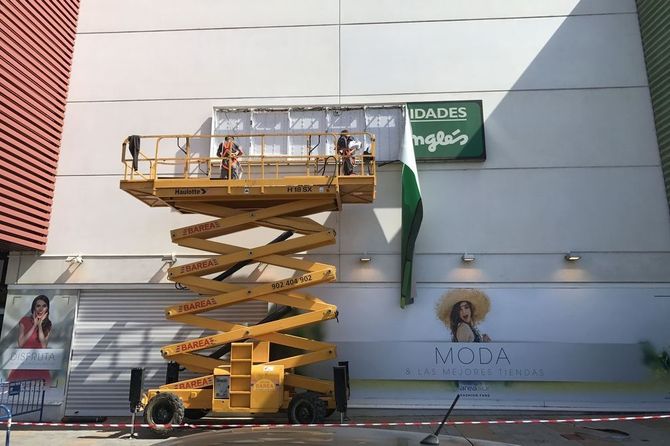 Se está utilizando un elevador de tijera amarillo para instalar un cartel en el costado de un edificio.