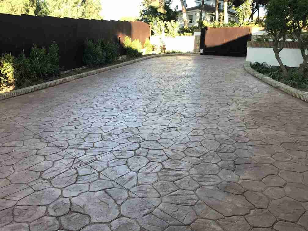 Un camino de entrada con un patrón de ladrillos y una valla al fondo.