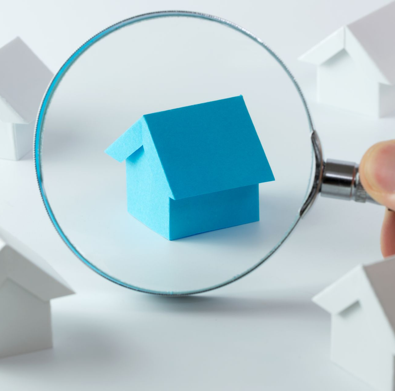 Loupe focalisant sur une petite maison bleue entourée de maisons miniatures blanches.