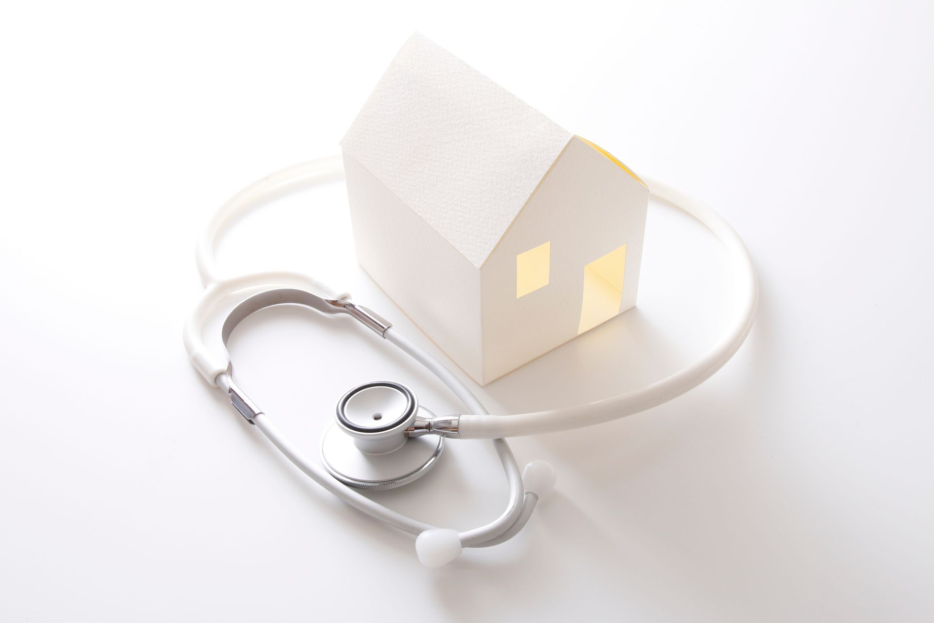 Maison en papier blanc entourée d'un stéthoscope, symbolisant la santé à domicile ou l'inspection de la maison.