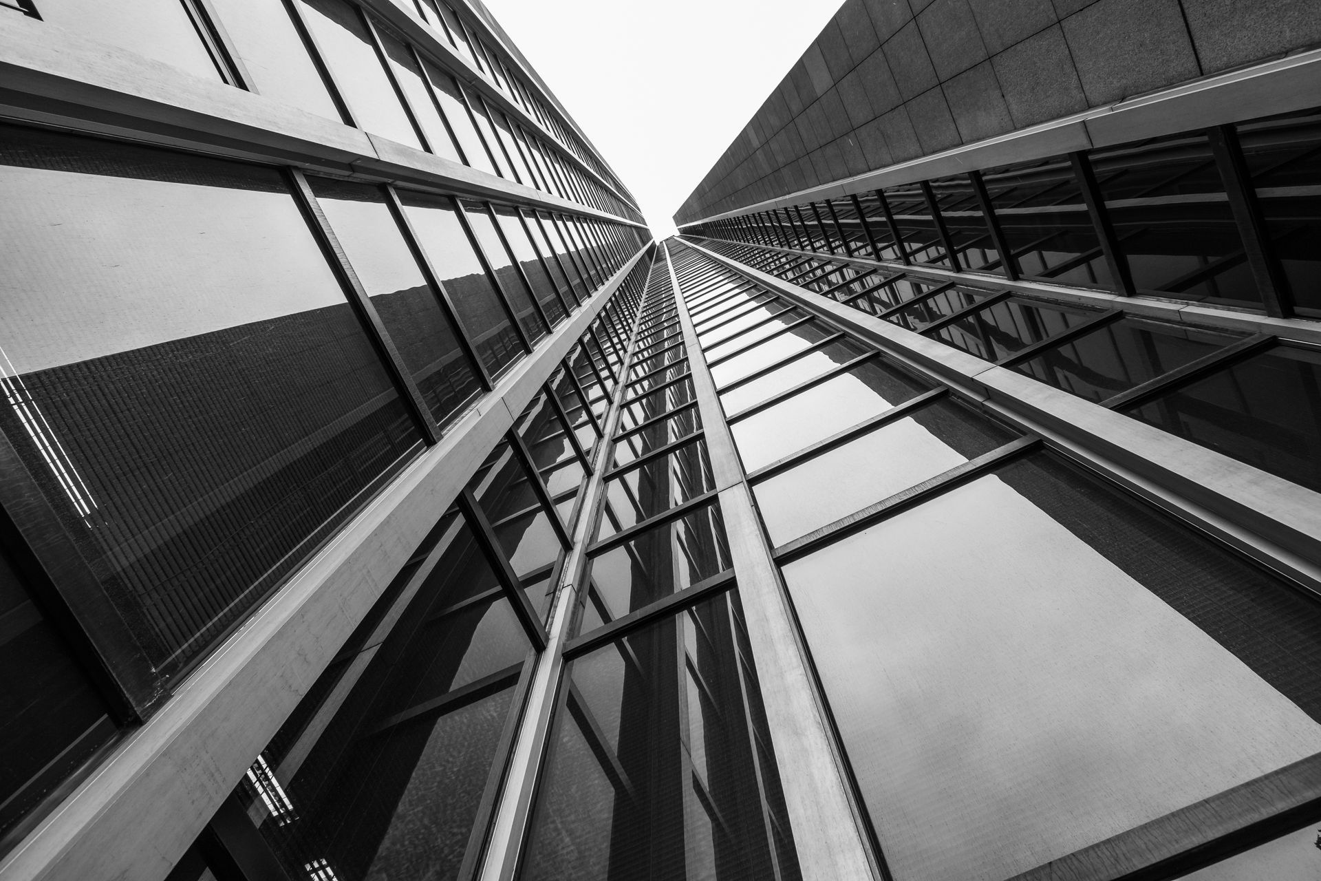 Vue en contre-plongée d'un grand gratte-ciel moderne aux nombreuses fenêtres réfléchissantes. Noir et blanc.