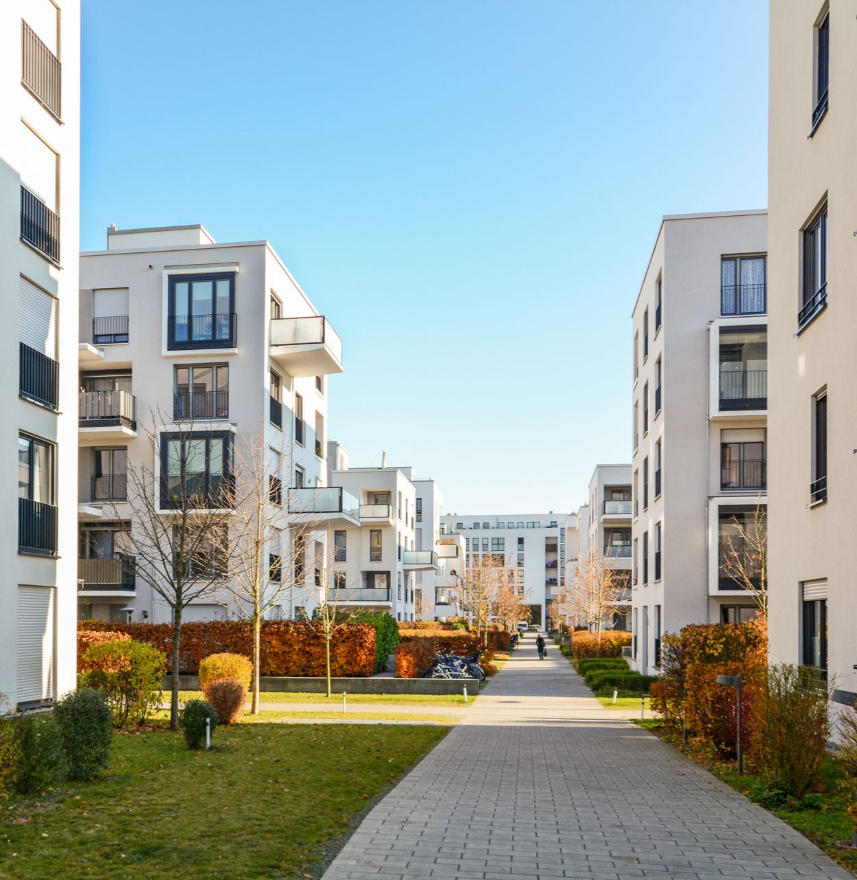 Immeubles d'appartements blancs modernes avec une passerelle et de la verdure par une journée ensoleillée.
