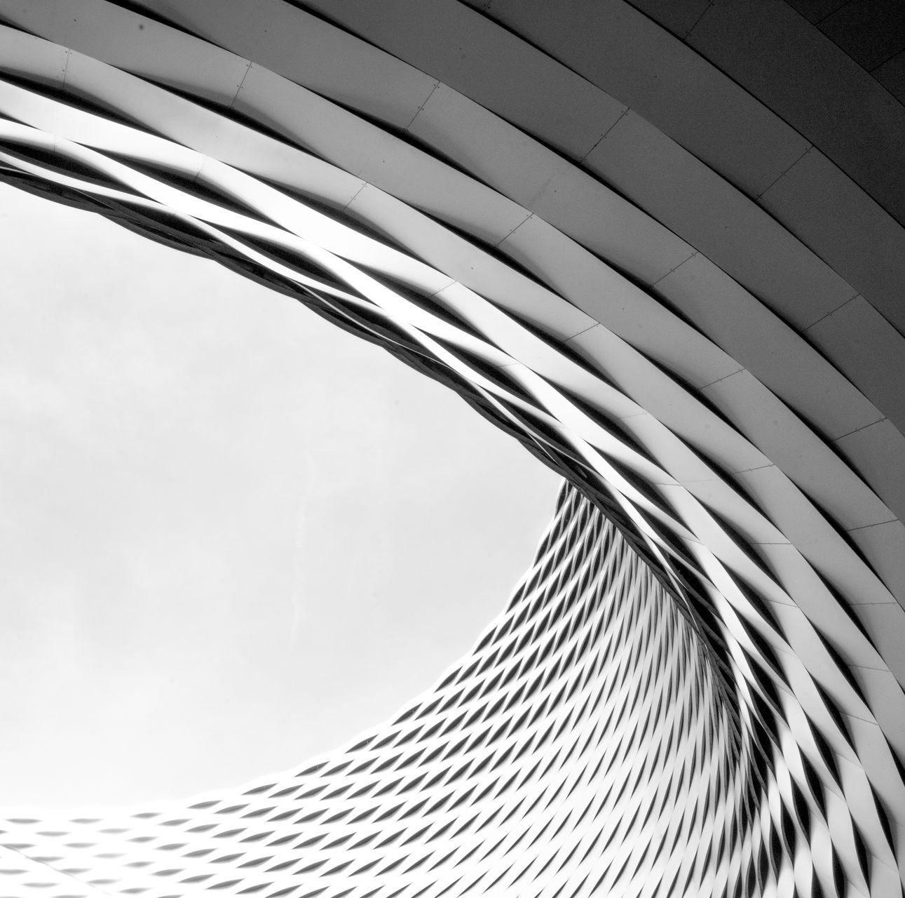 Prise de vue abstraite en noir et blanc d'une structure architecturale circulaire avec des motifs répétitifs en forme de losange.