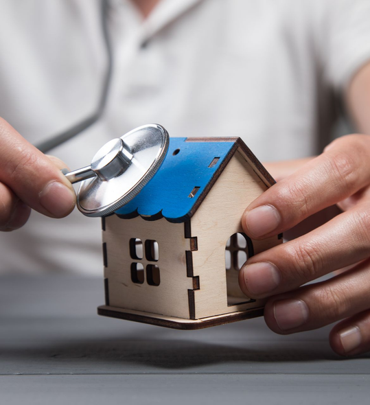 Mains tenant une maison miniature, utilisant un stéthoscope, impliquant une inspection de la maison.