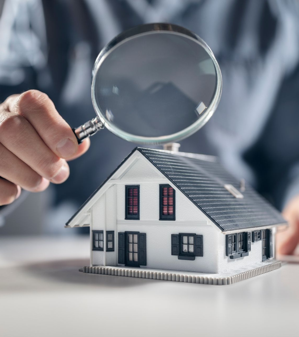Personne inspectant une maison modèle avec une loupe.