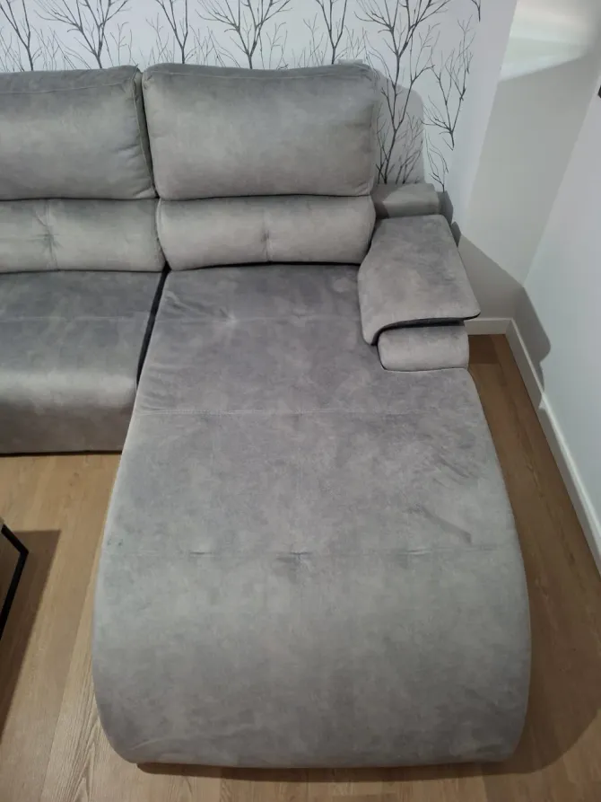Sofá modular gris con chaise longue en la esquina de una habitación, contra una pared clara y suelo de madera.