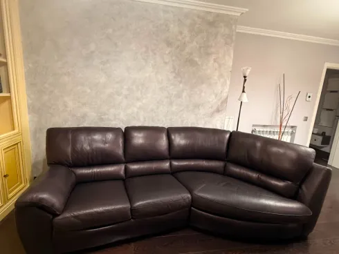 Sofá seccional de cuero marrón oscuro en una sala de estar con paredes beige y gabinetes dorados.