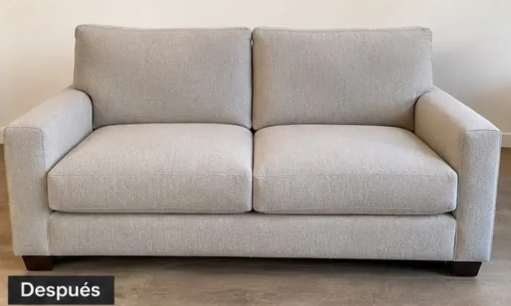 Sofá beige de dos plazas con cojines contra una pared lisa, con la inscripción