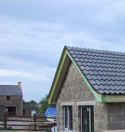 Une petite extension en parpaings est en construction à côté d'une maison plus ancienne, avec un nouveau toit en tuiles.