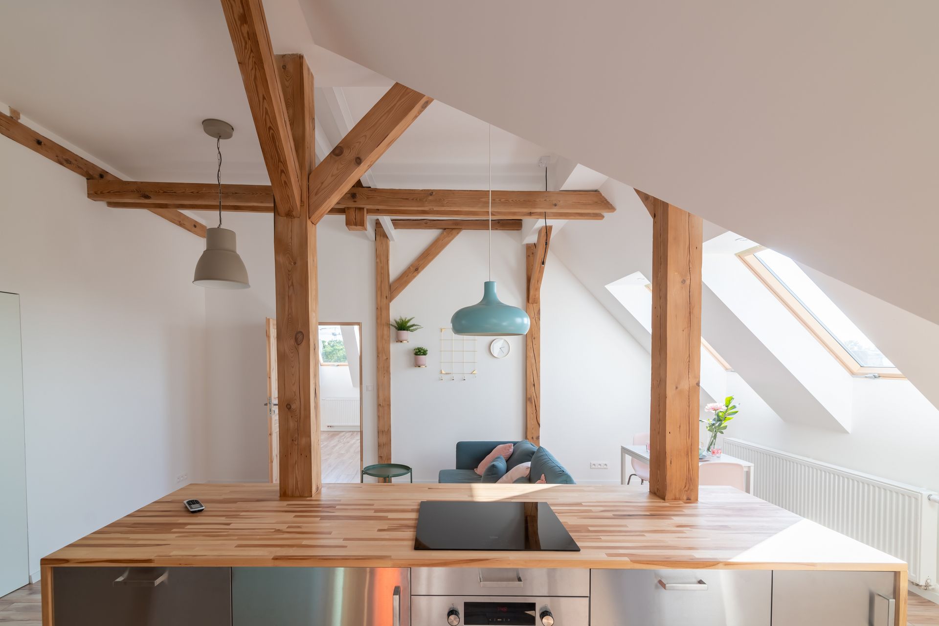 Cuisine lumineuse de style loft avec poutres apparentes, murs et puits de lumière, organisée autour d'un îlot en bois.