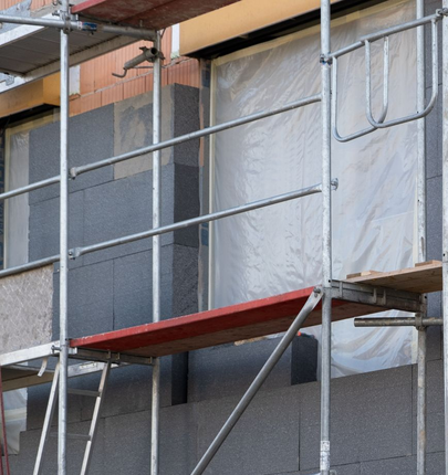 Façade d'un bâtiment en construction, avec échafaudages, isolation, briques et panneaux.