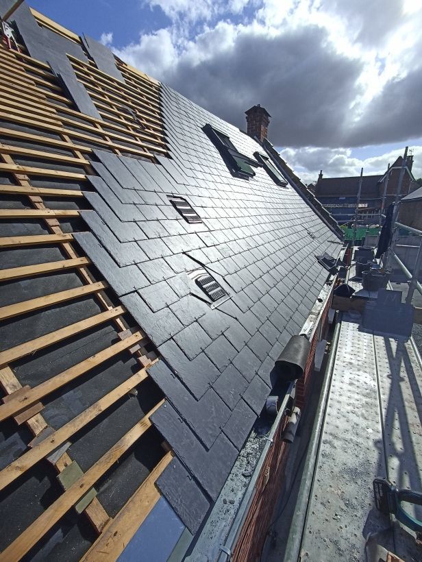 Toiture en construction avec des tuiles d'ardoise, des liteaux apparents et des ouvriers sur des échafaudages