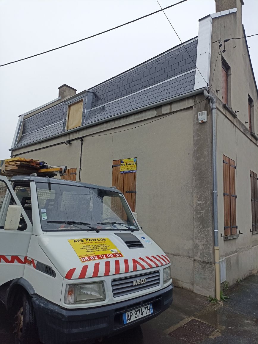Une camionnette utilitaire est garée à côté d'une maison avec un toit en pente recouvert de panneaux solaires.