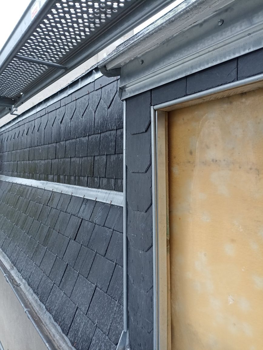 Mur extérieur en bardeaux, avec une bordure de toit en métal et un cadre de fenêtre recouvert de planches.