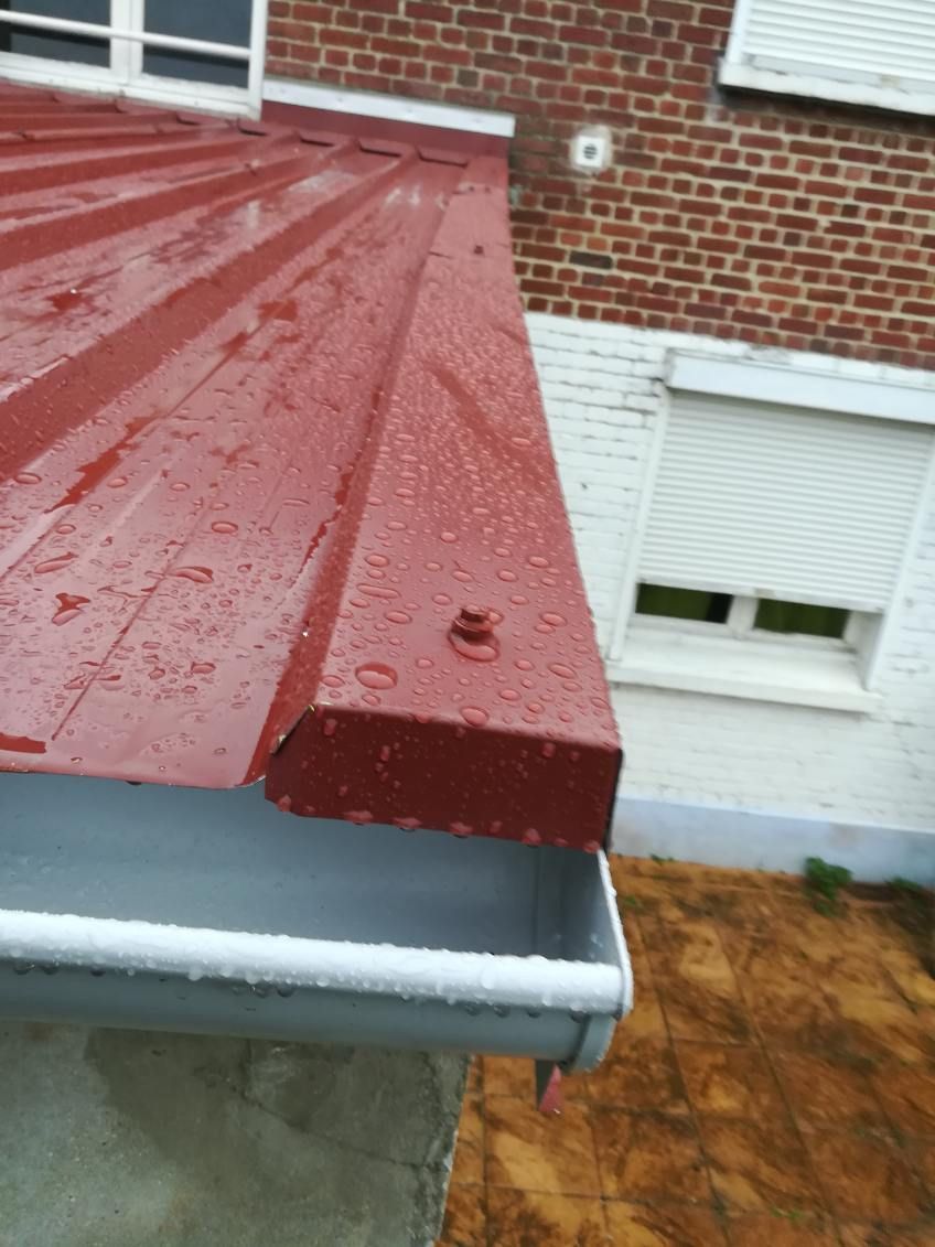 Bordure de toit en métal avec des gouttes de pluie contre un mur de maison en briques