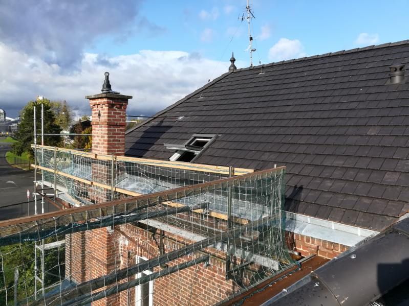 Toiture en rénovation avec échafaudages métalliques, toit de tuiles sombres et cheminée en briques