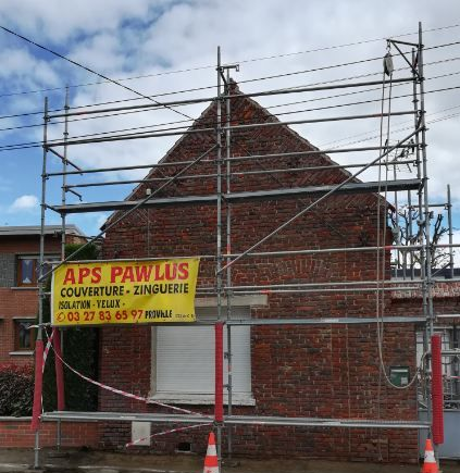Maison en briques sous un échafaudage, avec une banderole du chantier APS Pawlus.