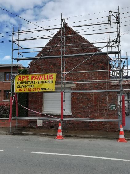 Maison en briques en rénovation, avec échafaudages, panneau et cônes de signalisation en bord de route