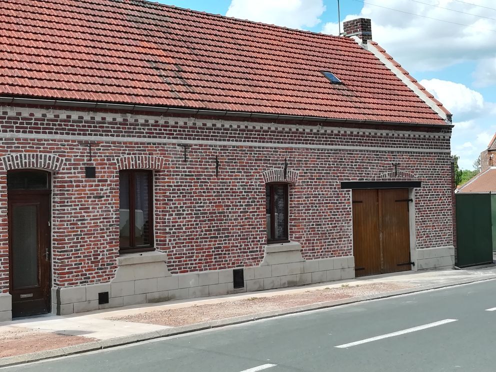 Maison en briques avec toit de tuiles et portes en bois, située dans une rue calme.
