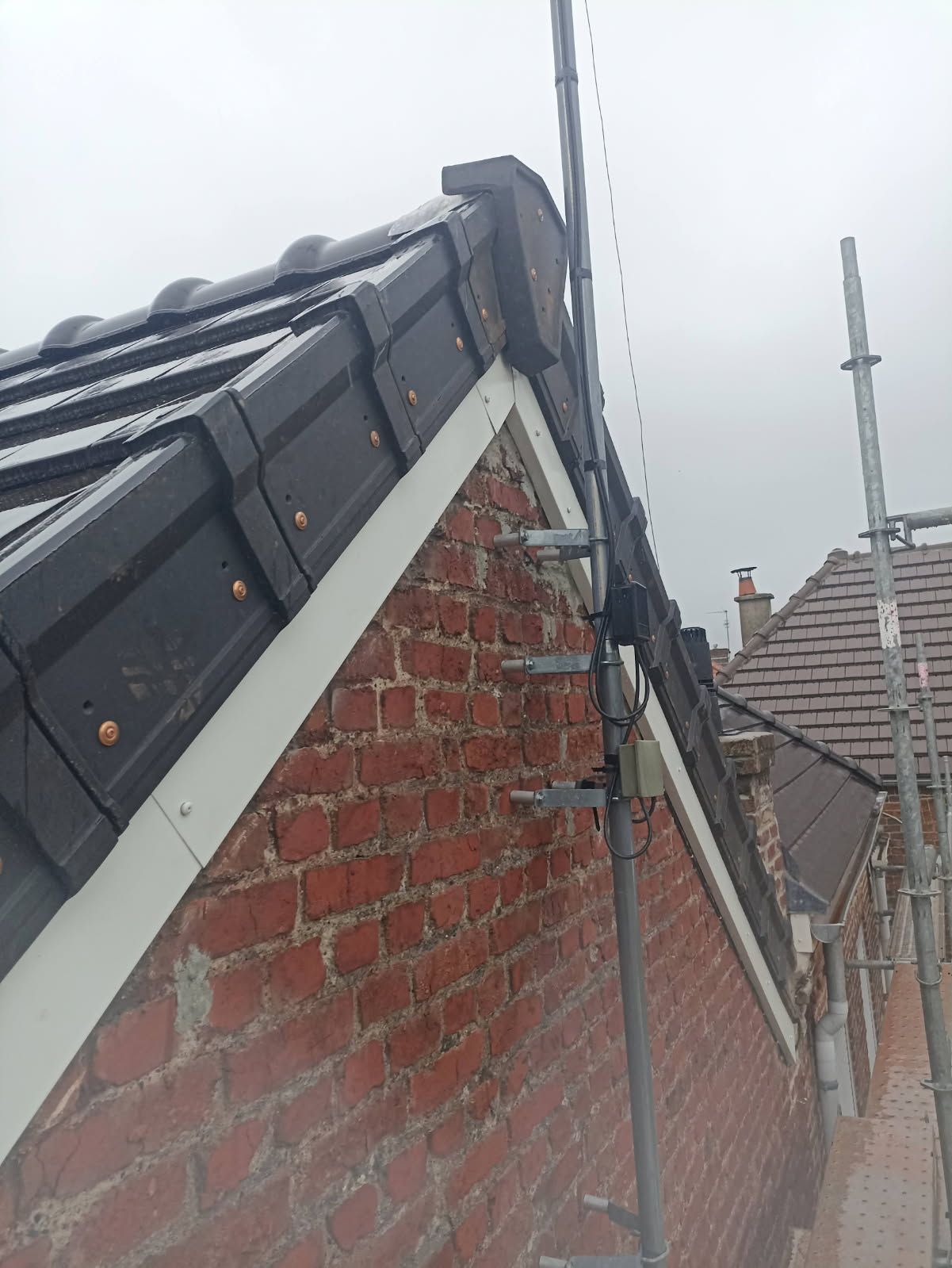 Bord de toit endommagé sur une maison en briques avec des tuiles descellées