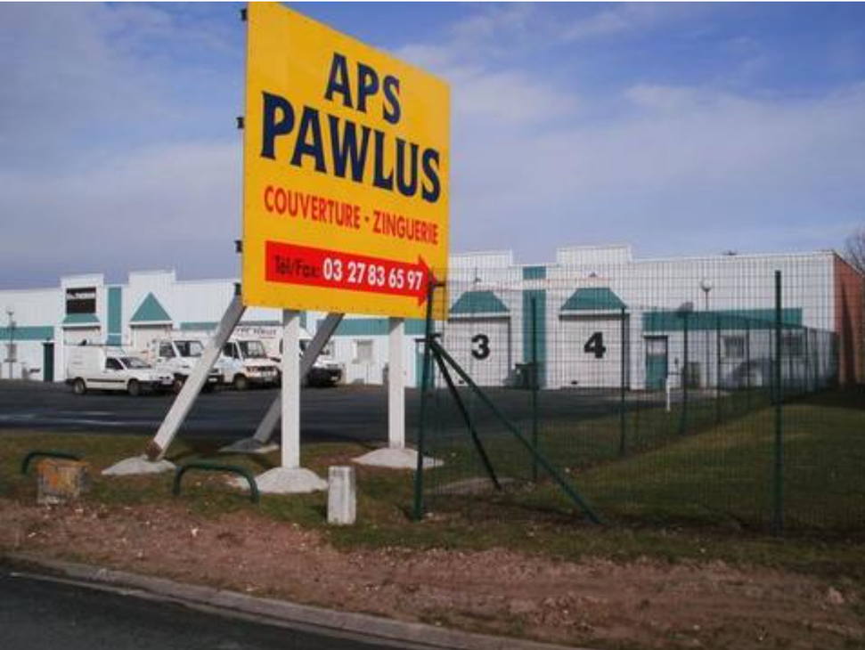 Panneau APS Pawlus devant des bâtiments industriels et des conteneurs de stockage