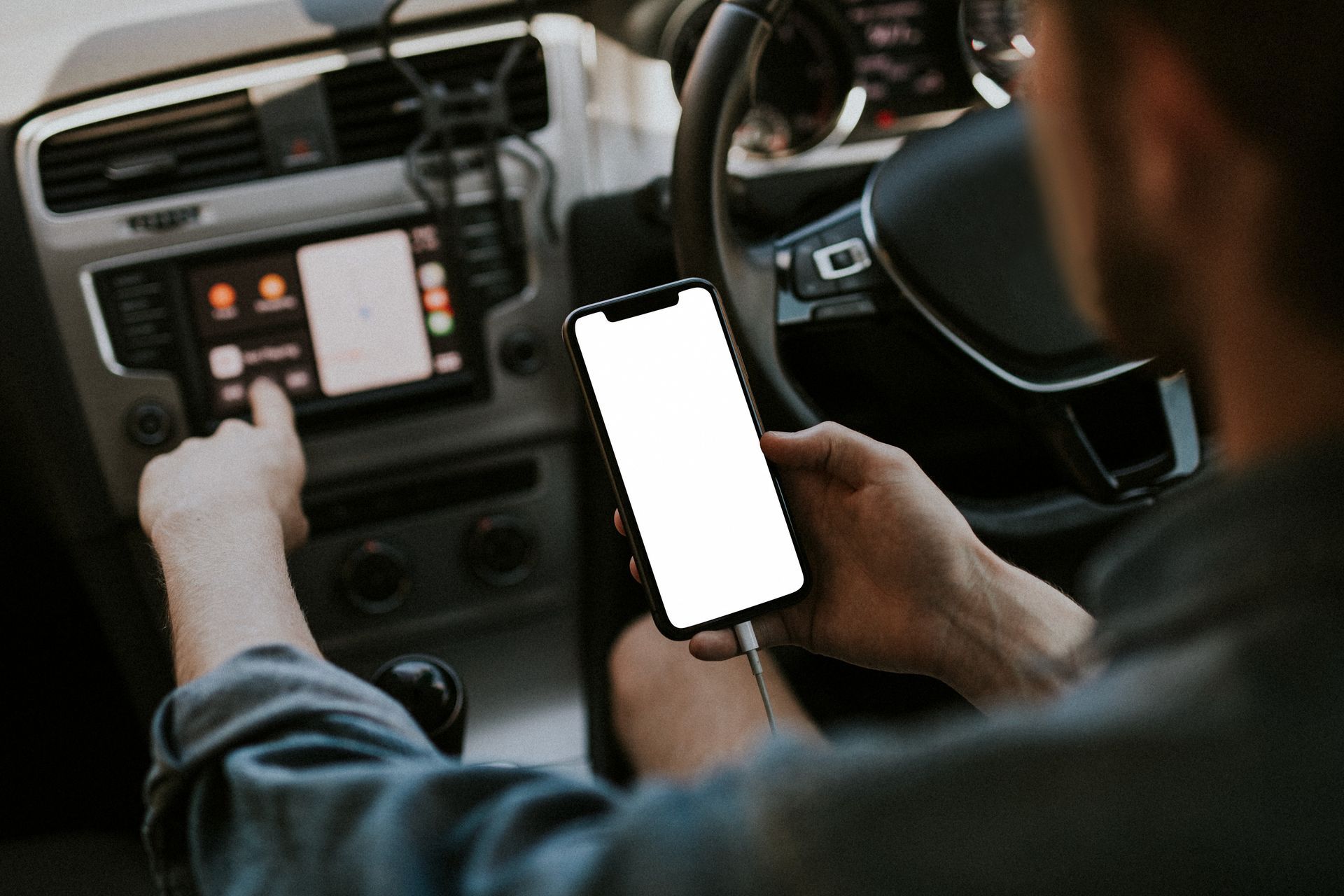 Une personne assise au volant touche l'écran de la voiture tout en tenant un téléphone.