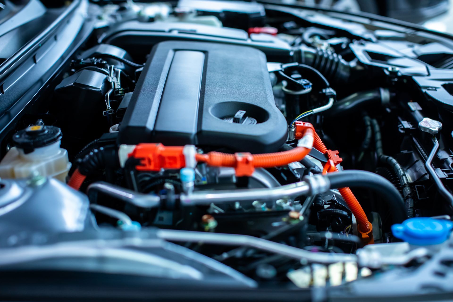 Gros plan sur un moteur de voiture avec des câbles haute tension orange bien visibles et un capot moteur en plastique noir.