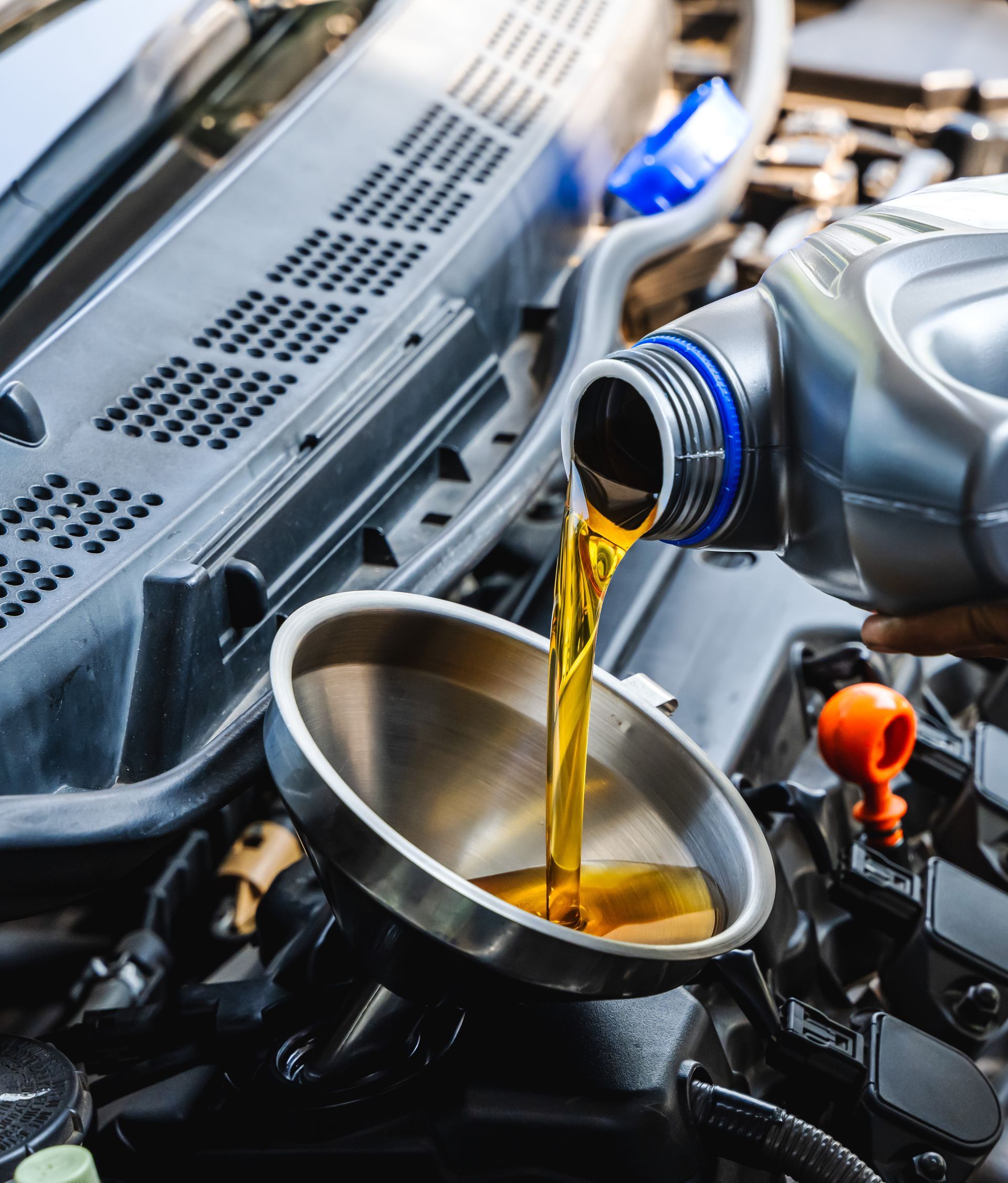 De l'huile moteur se déverse d'une bouteille en plastique dans un entonnoir en métal argenté.
