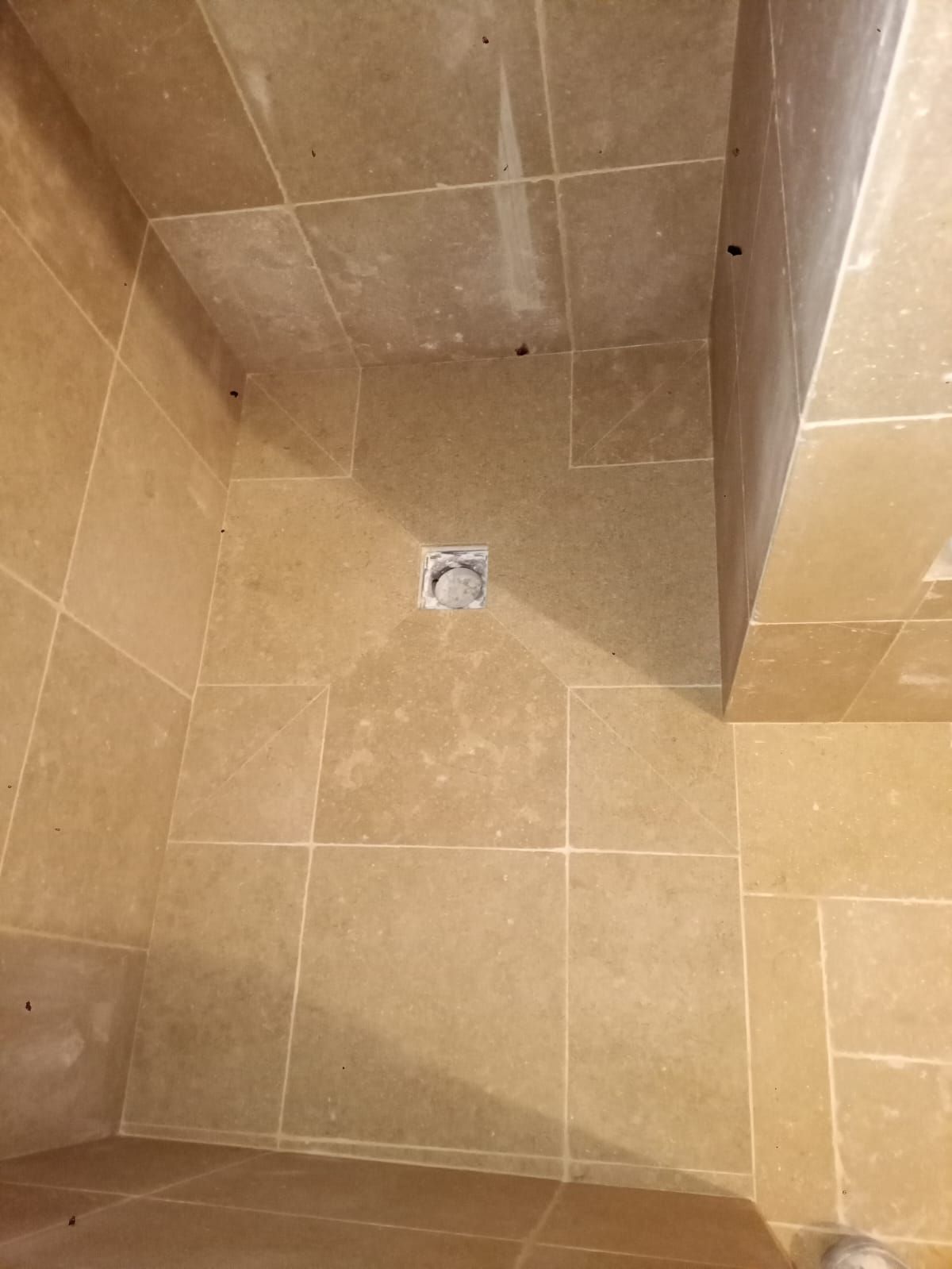 Cabine de douche carrelée beige avec bonde.