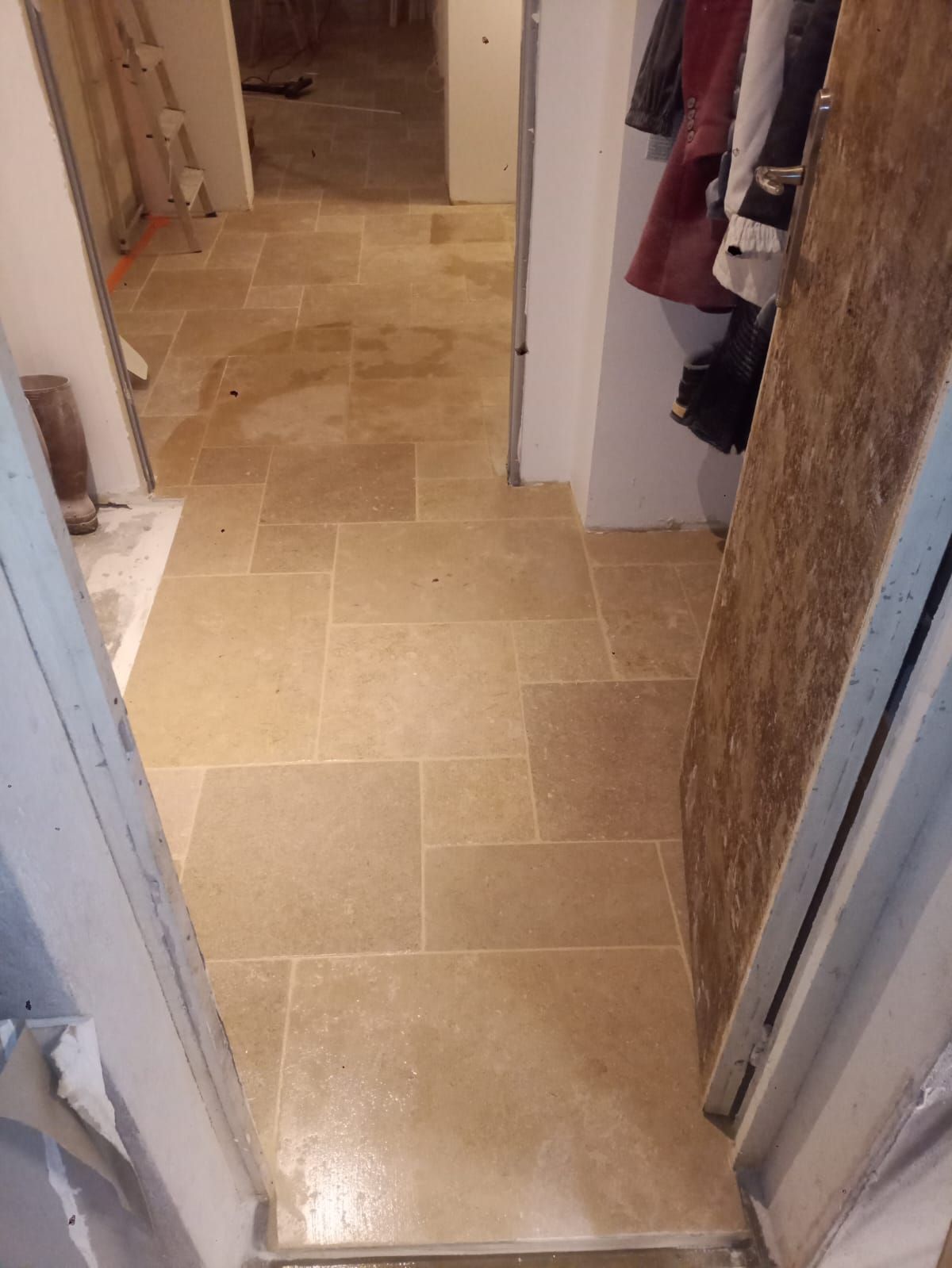 Carrelage en pierre beige posé dans un couloir avec une porte ouverte.