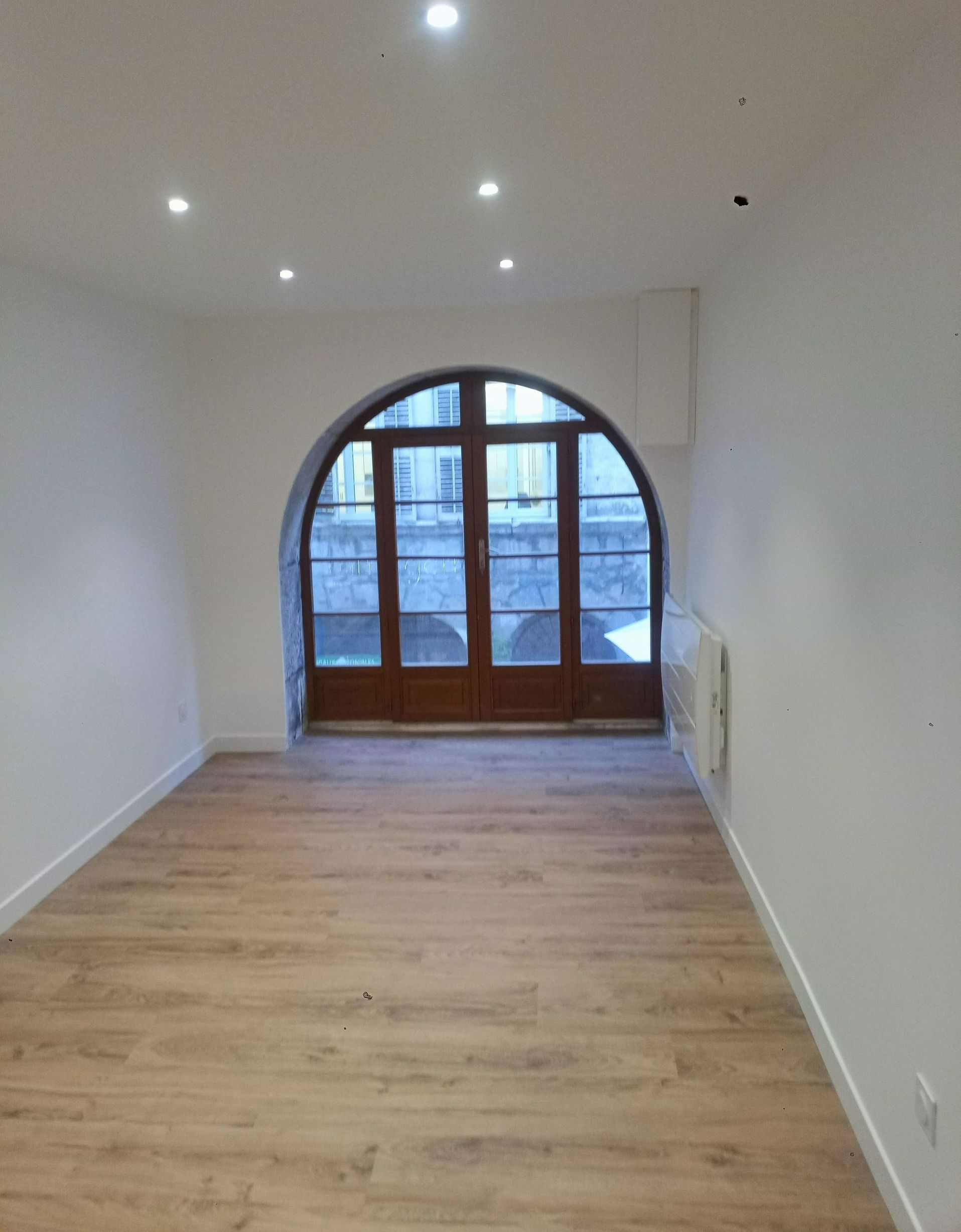 Pièce vide avec porte cintrée et parquet.