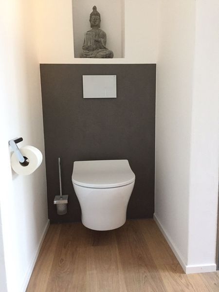 Modernes kleines Badezimmer mit wandhängendem WC, dunkler Akzentwand, WC-Bürste und Holzboden.