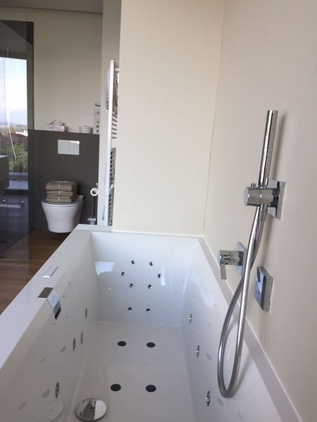 Modernes Badezimmer mit weisser, ebenerdiger Badewanne und verchromter Handbrause