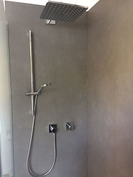 Moderne Dusche mit grauer Fliesenwand, quadratischem Regenduschkopf, Handbrause und Schlauch.