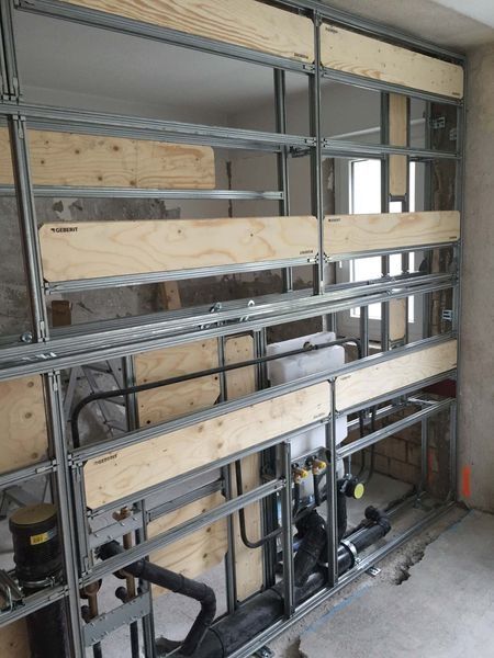 Unfertige Wandkonstruktion mit Metallständern, Sperrholzrückwand und freiliegenden Rohrleitungen in einem Baustellenbereich