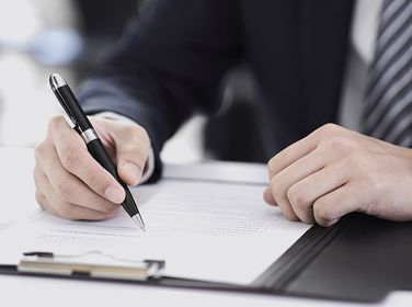 Un hombre está escribiendo en un trozo de papel con un bolígrafo.