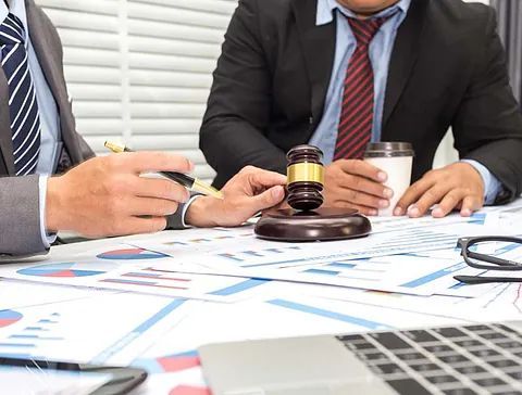 Dos hombres con traje y corbata están sentados en una mesa sosteniendo un mazo.