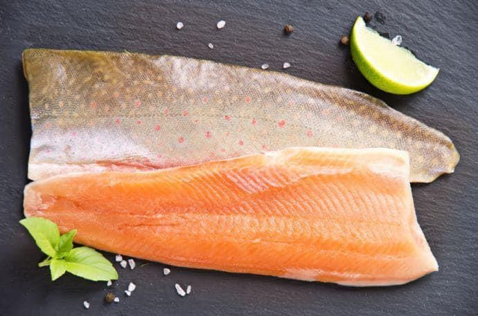 Ein Stück Lachs liegt neben einer Limettenscheibe auf einem Tisch.