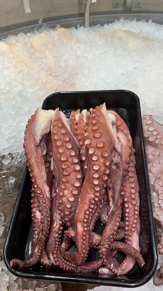 Ein schwarzes Tablett gefüllt mit Tintenfischtentakeln auf Eis.