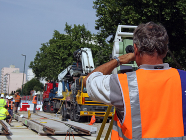 Équipe de travaux publics et camion-citerne à ciment dans une rue de la ville, avec des ouvriers portant des gilets de sécurité orange.