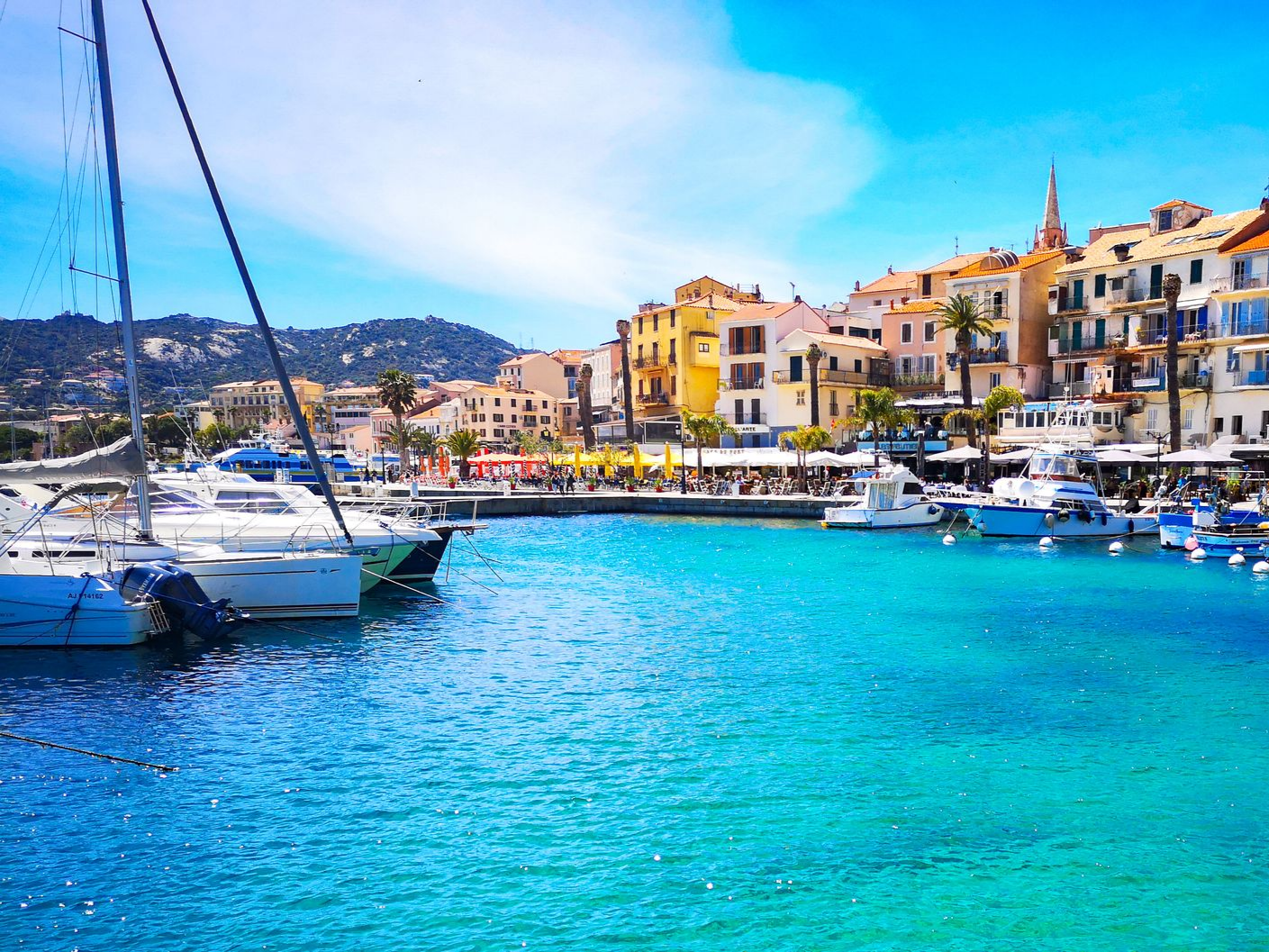 Port balnéaire coloré avec ses voiliers, son eau turquoise et ses bâtiments aux couleurs pastel le long du rivage.