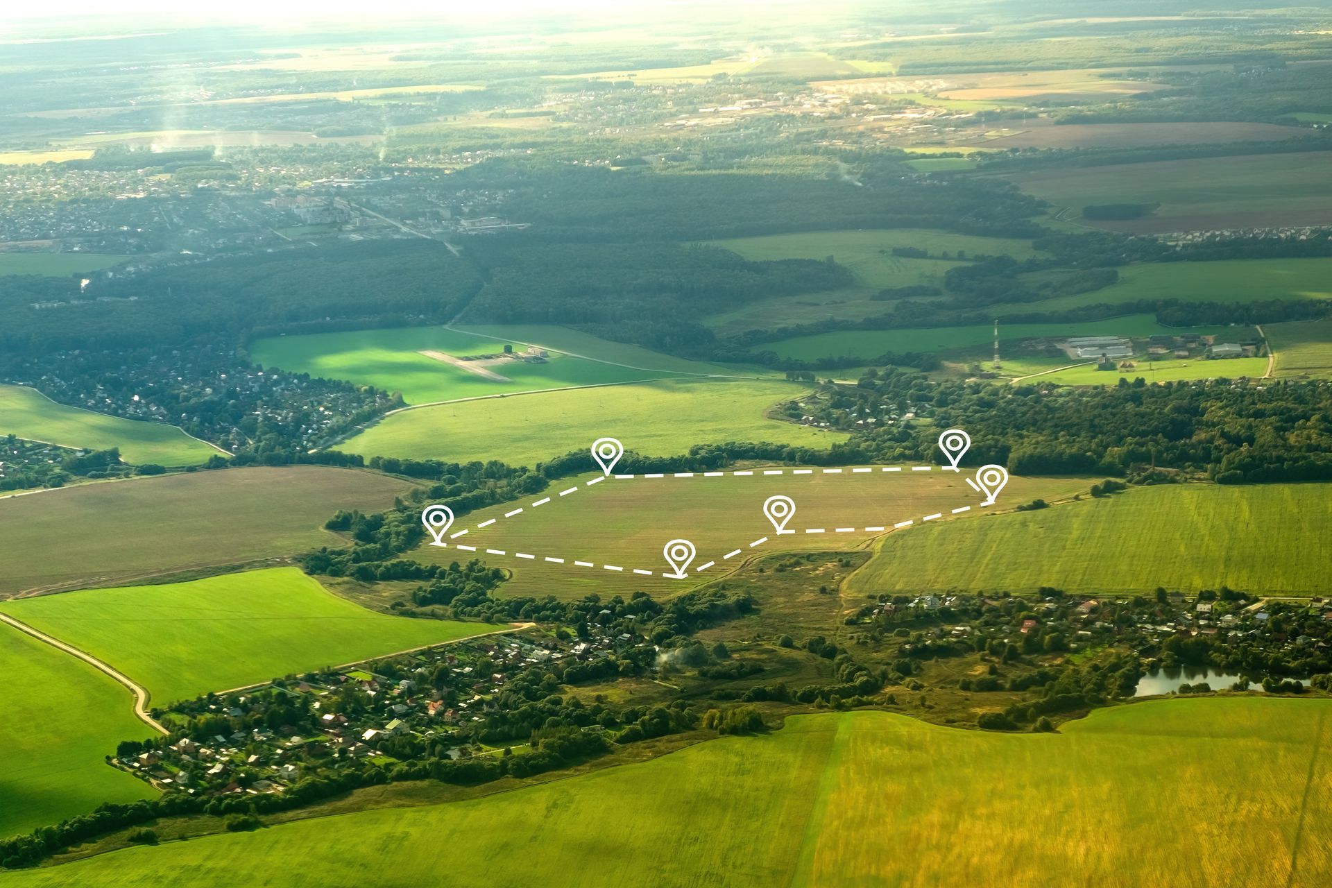 Vue aérienne de terres agricoles verdoyantes avec un chemin en pointillé marquant la limite d'un champ.